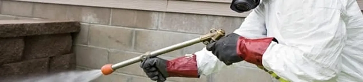 Pest control technician applying exterior insect treatment along a home foundation in Miami, FL