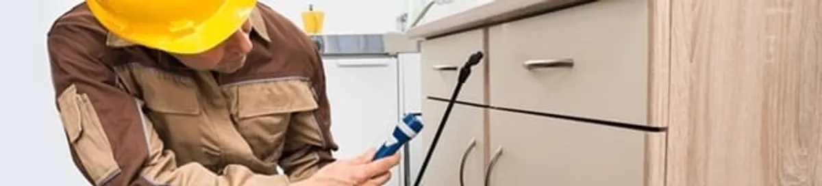 Roach exterminator applying treatment under kitchen cabinets in Miami, FL