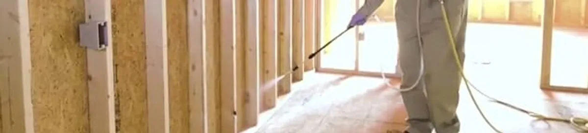 Termite treatment technician applying spray along framing and unfinished walls in Miami, FL